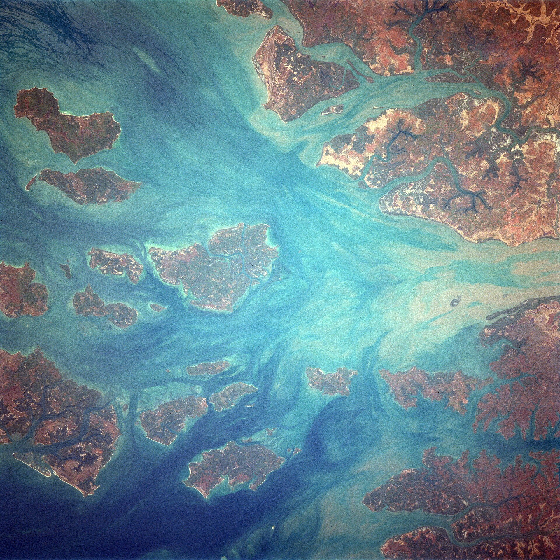A view from space of the Bijagós islands: dark green and rust-coloured islands scattered in turquoise, silt-streaked water.