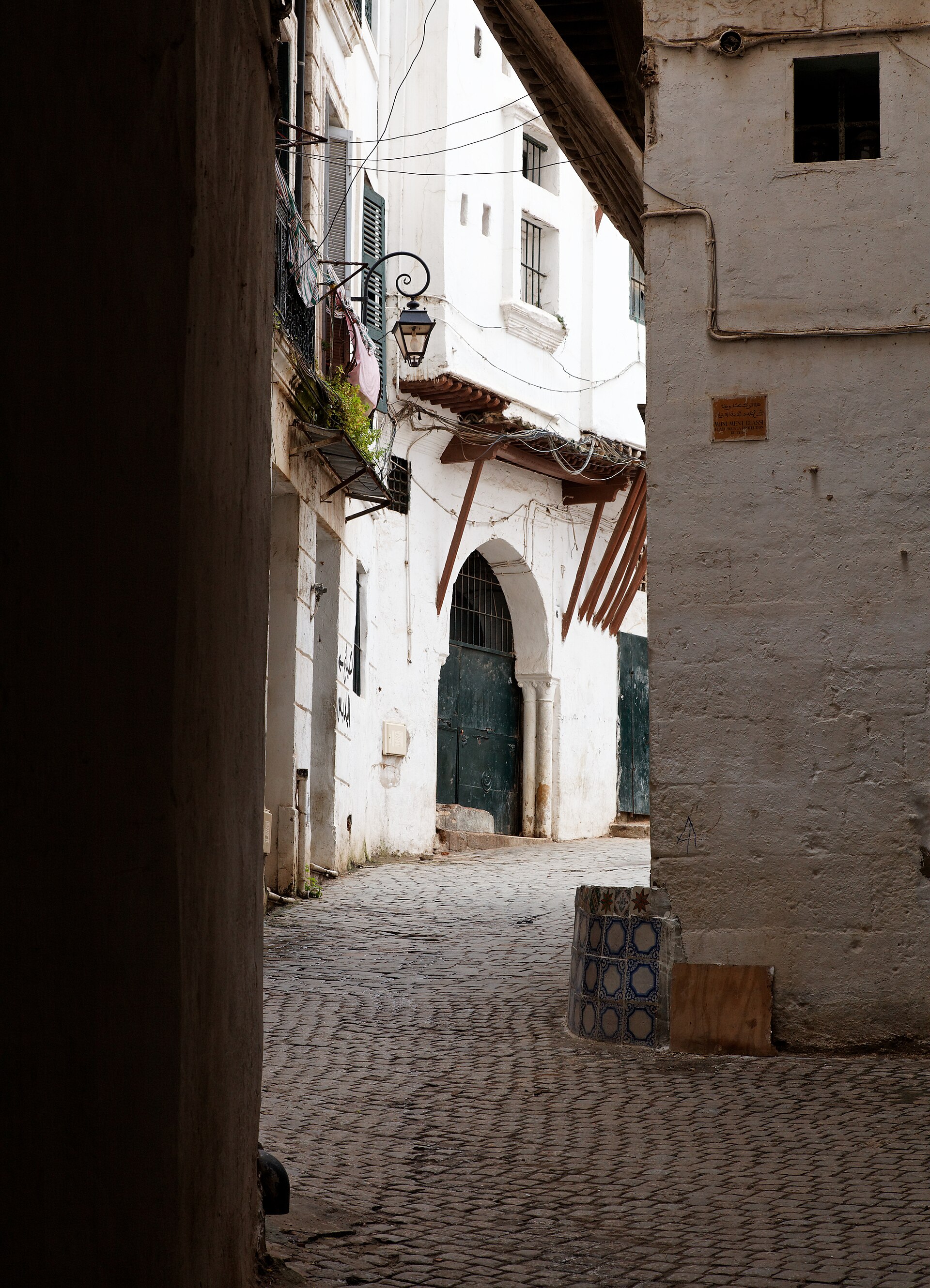 A narrow lane in the Casbah of Algiers, with a white wall and an arched doorway.