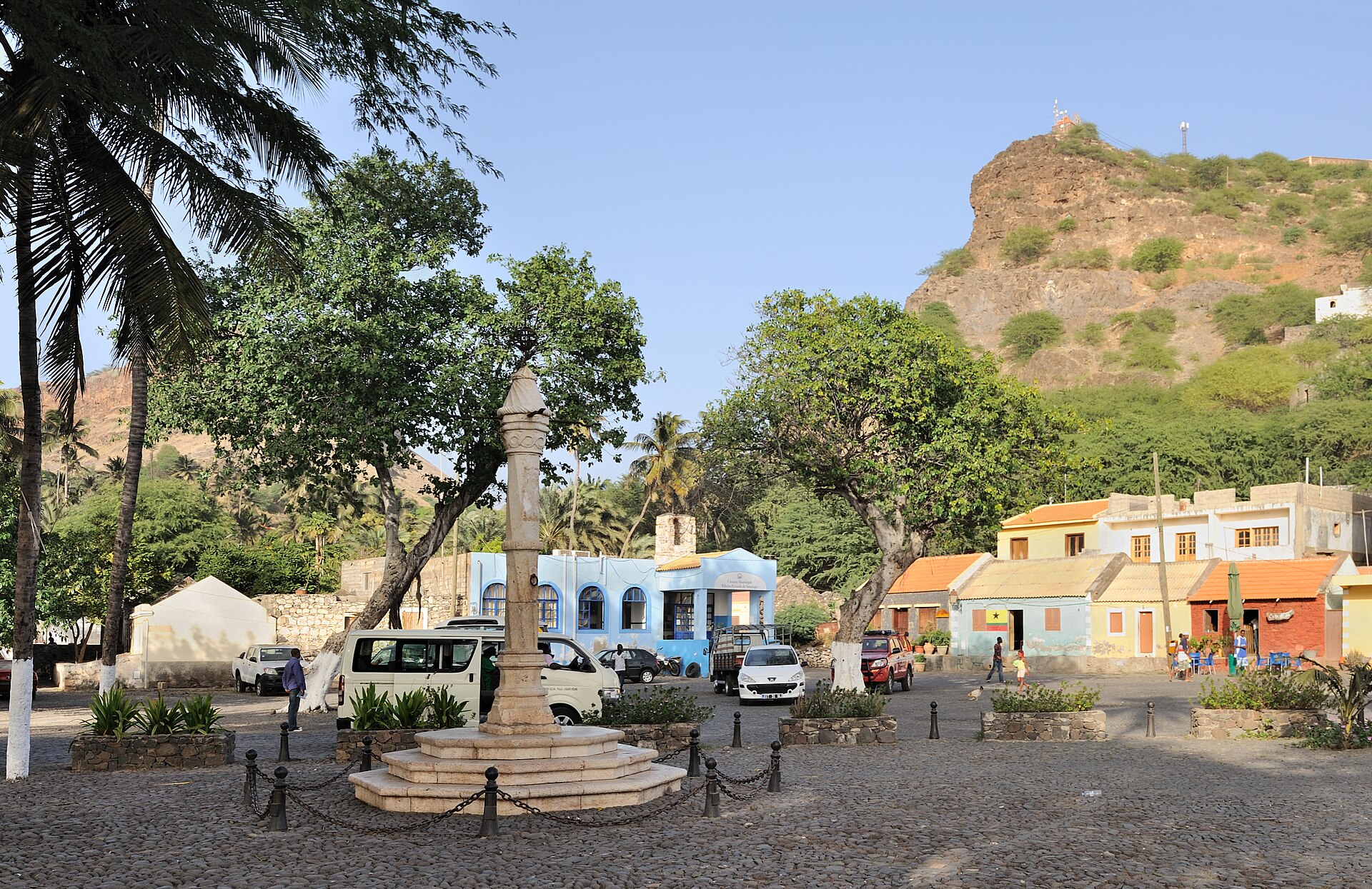 A small square in Cidade Velha with the stone pillory, low colonial houses and hills behind.