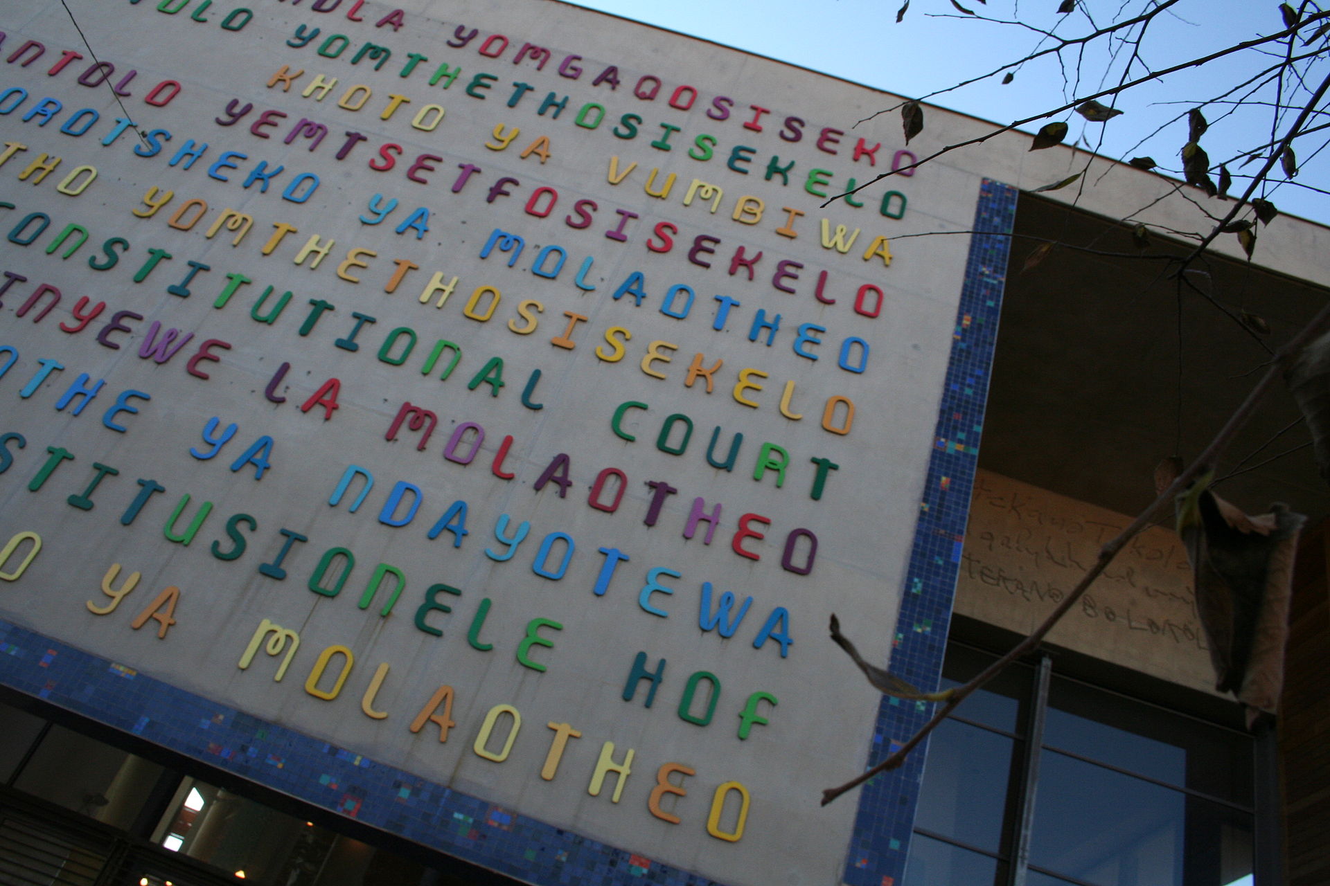 A wall at the entrance of the Constitutional Court covered with rows of coloured letters, with a blue tiled border.