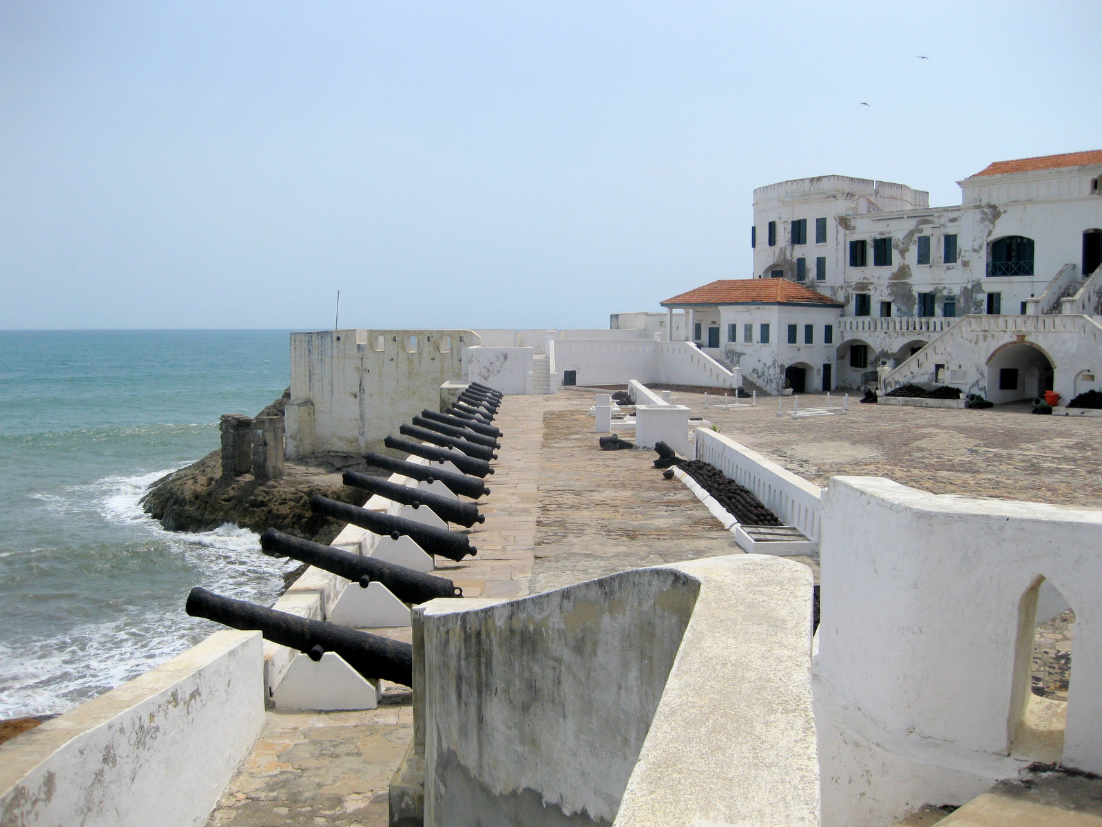The white walls and cannon of Cape Coast Castle above the shore.