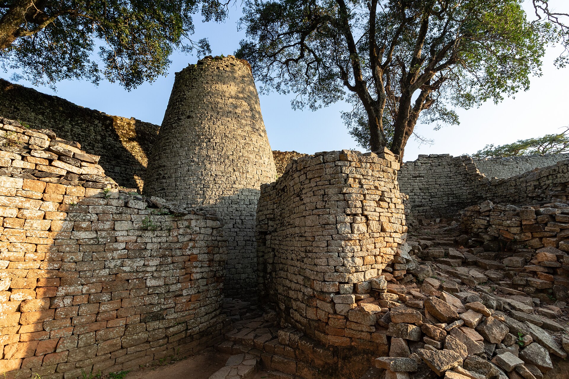 A conical dry-stone tower and stone walls inside the Great Enclosure, with trees behind.