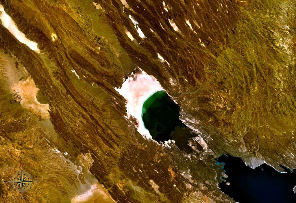 Satellite view of Lake Assal: a dark green lake with a pale salt shore among brown, ridged terrain.