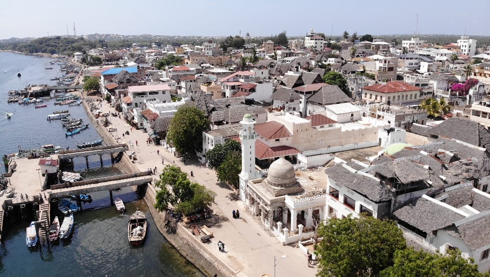 An aerial view of Lamu town, with white buildings, a mosque and boats along the waterfront.