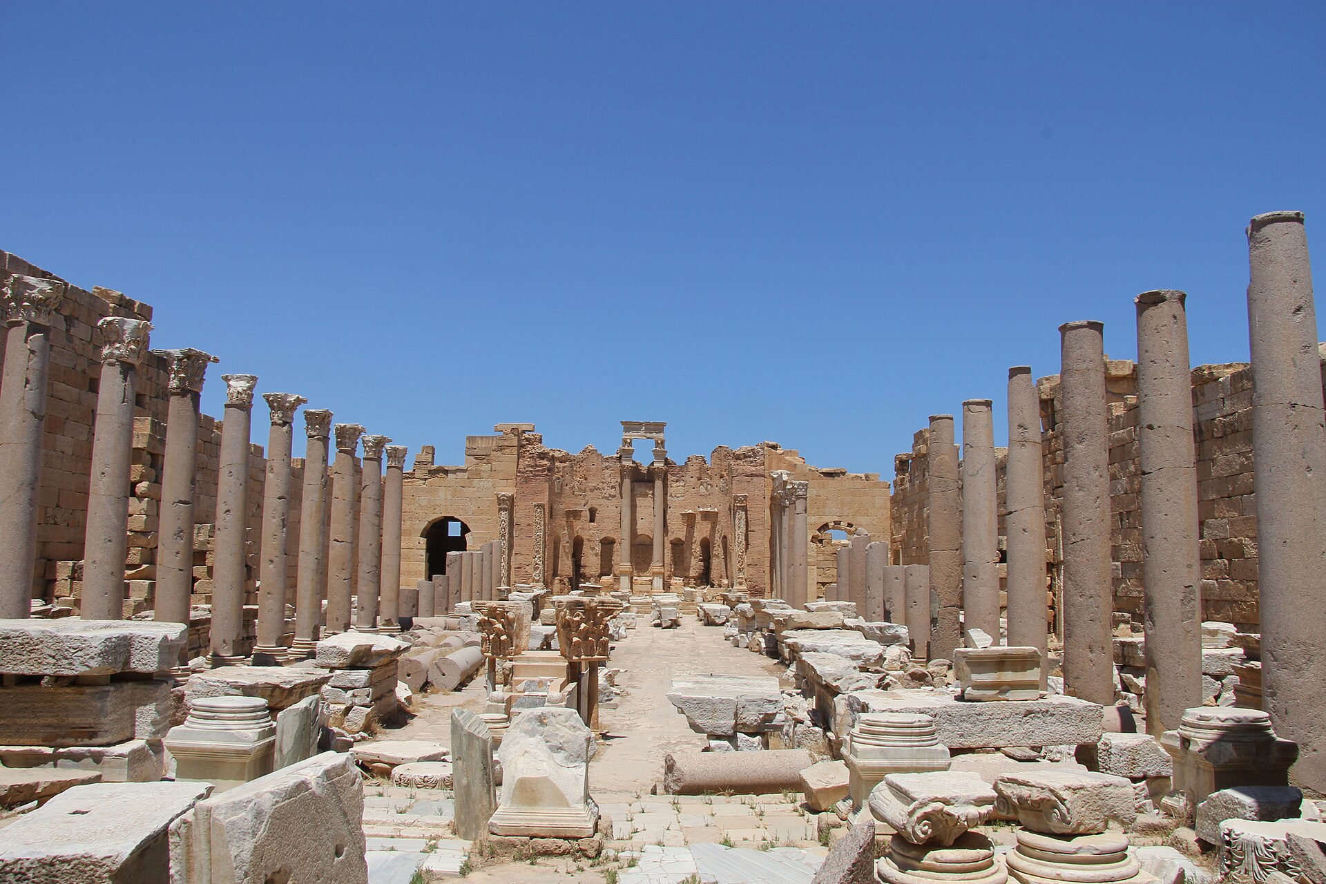 Rows of tall stone columns along a paved street among the ruins of Leptis Magna, under a blue sky.