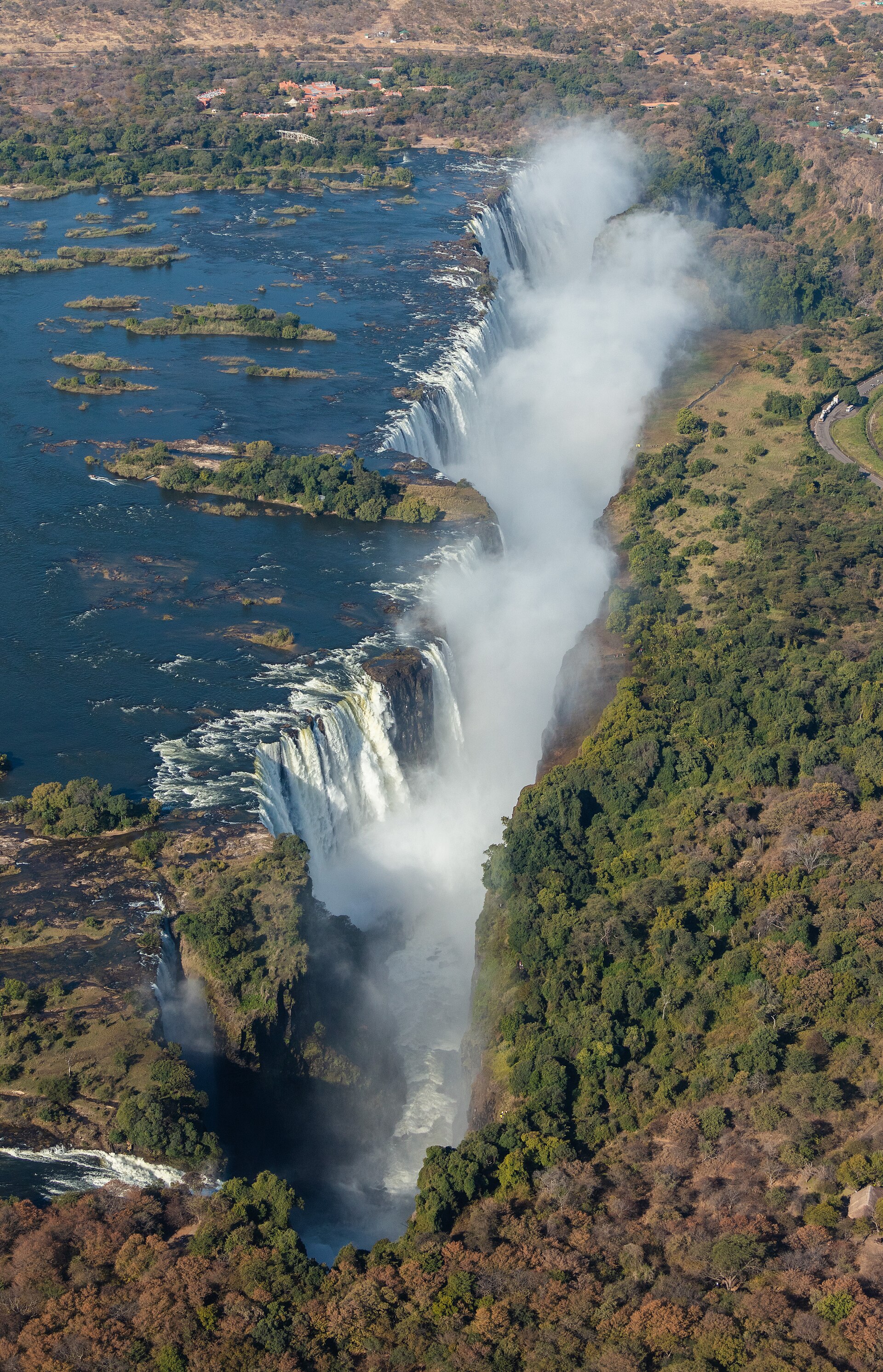 An aerial view of Victoria Falls, with water dropping into a gorge and green forest on both sides.