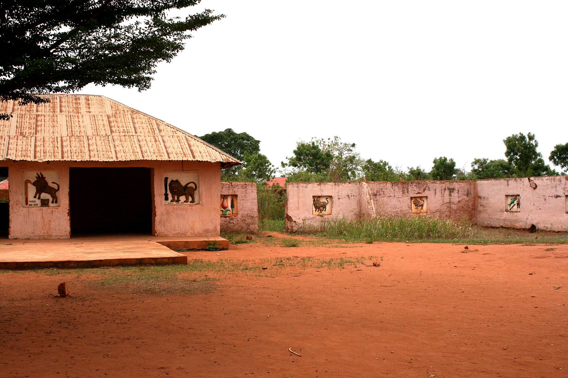 A long, low palace building in Abomey with earthen walls and a roof, seen from across a sandy courtyard.